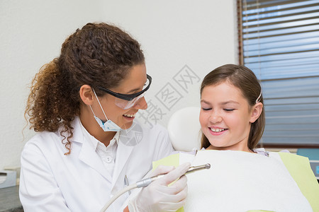 儿科牙医在椅子上与小女孩笑着微笑口腔科女孩设备医学口腔诊所口罩牙钻保健快乐背景图片