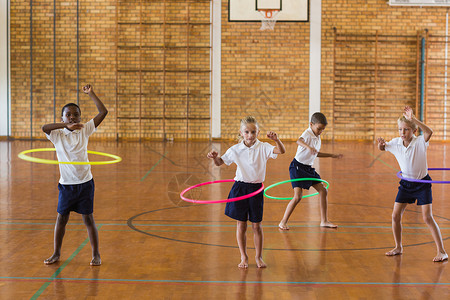 学生在学校体育馆玩hula hoop闲暇体育男性校园小学教育女学生木头大厅地面背景图片