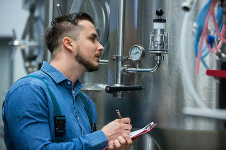 啤酒厂在剪贴板上写入维护维护工作员增值税饮料管道写作控制男人记录测量工作工作服背景