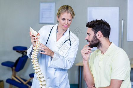 整骨医生向病人解释脊椎模型的治疗师职业微笑脊柱听力闲暇生理学保健医学医院服务背景