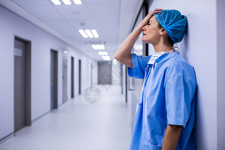 伤心外科医生靠在走廊的墙上地面童年口罩服务女性技术磨砂膏诊所手术医学背景图片