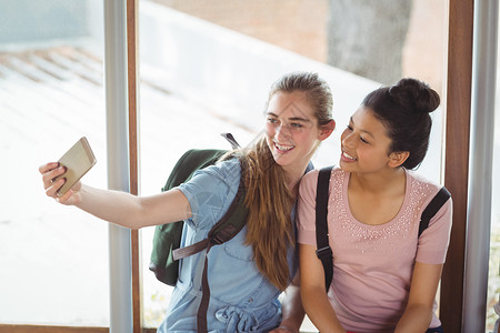 快乐的女学生在走廊上用手机自拍朋友学校微笑门厅友谊技术教育学生服装享受背景图片