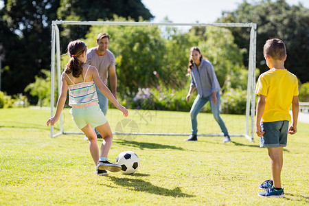 踢足球的女孩家庭在公园一起踢足球的比赛晴天女儿游戏喜悦服装跑步孩子母亲女士享受背景