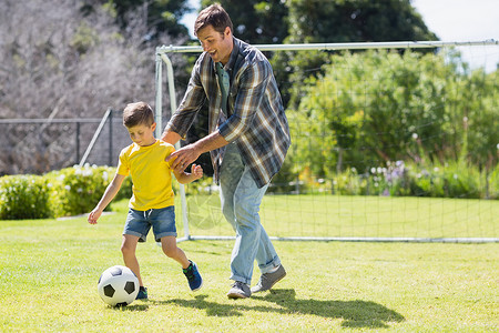 父亲和儿子在公园踢橄榄球快乐男人孩子足球男生服装微笑感情现实门柱背景图片