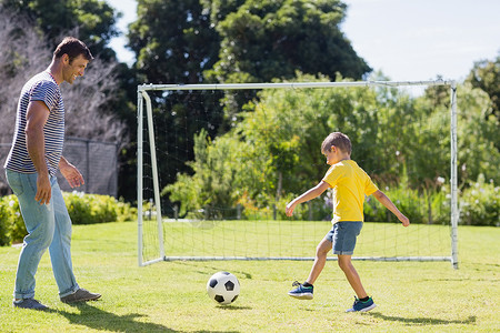 一个足球素材父亲和儿子在公园踢橄榄球守门员微笑休闲童年花园喜悦草地服装假期男人背景