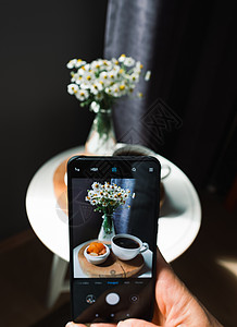 手机相片素材手持智能手机拍摄一杯咖啡的相片 家里附近有鲜花背景