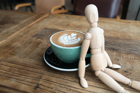 卡人模型人热辣咖啡或茶杯中的卡普奇诺 由木匠靠在绿色的杯子上模型男人身体姿势木偶娃娃咖啡木头数字绘画背景