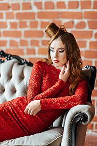 可爱灿烈红头发的年轻女孩 在明亮的房间穿着烈红礼服红色发型裙子化妆品美丽沙发女士女性微笑工作室背景
