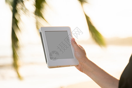 无线的棕榈树女性在海边户外拥有电子阅读器 其背景是棕榈树 在旅行中放松并享受着在户外阅读最喜欢的书籍青少年酒店闲暇电脑读者女孩日落触摸屏屏幕背景