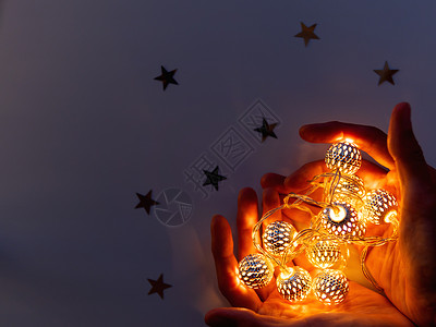 以心脏形状的手举着灯泡 金属灯泡星星魔法图案手势反射黑暗纸屑浪漫假期装饰品背景图片