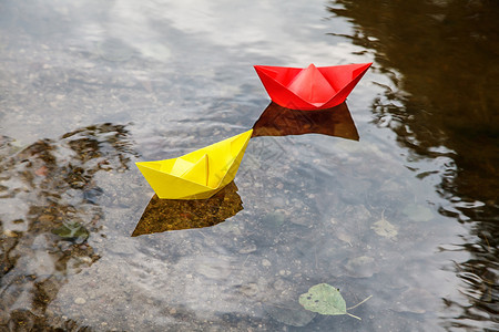 小纸船两艘多色纸船漂浮在溪流上乐趣折叠舰队池塘女性公园自由团体玩具季节背景