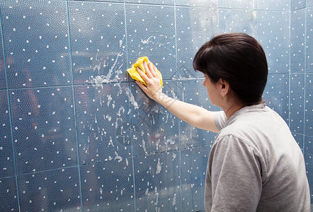 女人用布衣罩洗墙壁的瓷砖高清图片