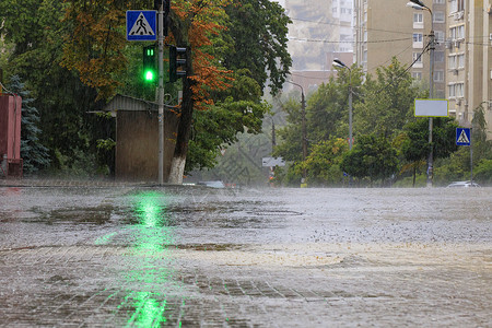 滂沱在人行道和柏油路的大雨被绿色红绿灯照亮液体建筑物反射天气波纹地面住宅气候房子倾盆大雨背景