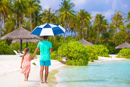 雨伞为孩子遮风挡雨的父亲父亲和小女孩带着雨伞躲在海滩的阳光下情调爸爸支撑海岸线阳伞海洋天堂家庭太阳日光浴背景