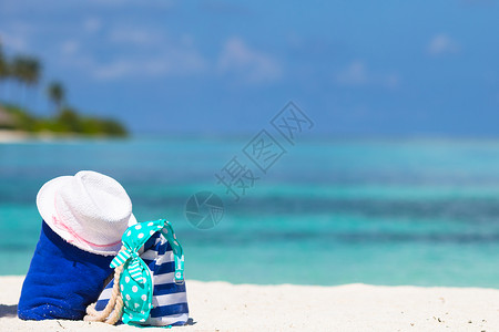 蓝色帽子白沙滩上的条纹袋 蓝毛巾 太阳墨镜 防晒霜瓶和泳衣太阳享受海滩旅游帽子稻草配饰娱乐支撑泳装背景