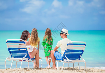 加勒比人暑假期间在海滩上快乐的家庭日光妈妈女儿爸爸海岸男人躺椅海滨享受女孩背景
