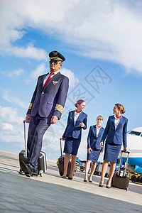我行走在空中与三名年轻的美丽空服员在机场对着飞机行走的成熟飞行员肖像 该机行李职业服务飞机场下载服务员工作旅行队长畅销书背景