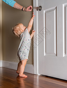 刚能走路的小婴儿伸手去拿木地板上的门把手孩子女士成人房子脚尖房间监视器童年手表安全背景图片
