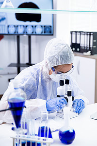 保护设备中的科学家妇女调整其显微镜;女科学家高清图片