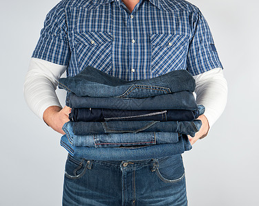 男人穿着牛仔裤和蓝色格子衬衫 拿着一堆牛仔裤身体展示纺织品裤子男性白色衣服工作室背景