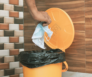 医用垃圾桶手将医用面罩扔进封闭的垃圾箱 — Covid-19 建议在使用后丢弃或将医用面罩扔进封闭的垃圾桶 — 表明要进行卫生实践的概念背景