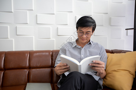 亚裔老人在家中客厅的沙发上读书 亚洲老年男子的肖像 正在放松和幸福与阅读杂志图片
