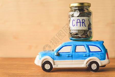 装有汽车标签和木制桌子上的汽车玩具的玻璃罐中的硬币现金高清图片素材