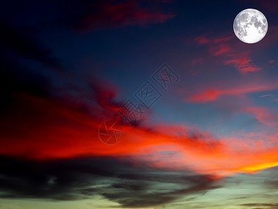 满月在色彩多彩的天空橙色和暗灰云上背景图片