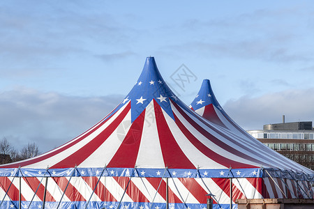 红色旗帜组合红白相间的马戏团帐篷 顶上是蓝星覆盖 顶着阳光明媚的蓝天 云朵狂欢乡愁闲暇吸引力圆顶蓝色喜悦横幅条纹派对背景