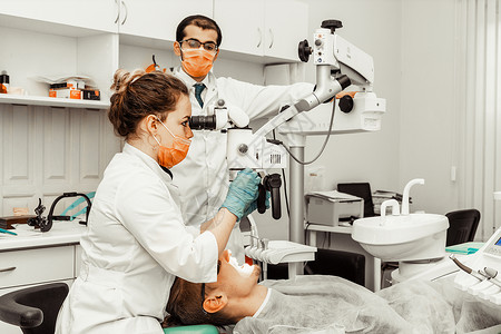 牙科技师精致两个牙医治疗一个病人 牙医的专业制服和设备 医疗保健装备医生工作场所 牙科程序女性镜子牙疼卫生工具治愈医学诊所女士背景