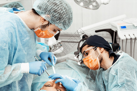 牙科技师两名男牙医为一名病人做手术 牙科外科 牙医的专业制服和设备 医疗保健装备医生工作场所 牙科女士治疗药品假牙镜子医学卫生员微笑牙科背景