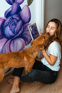 拿着画笔狗艺术家 设计师 宠物 年轻的女艺术家在室内的墙上作画 和狗一起工作和玩耍 宠物疗法 室内设计 创作过程职业画笔调色板刷子快乐乐趣背景