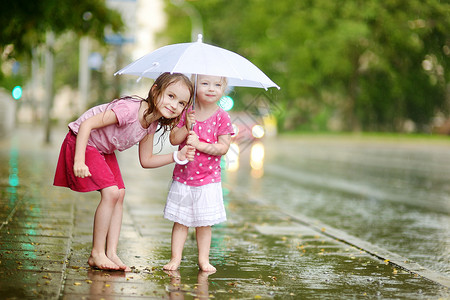 两个可爱的小妹妹 在雨下玩得开心自由朋友们乐趣水坑城市团队享受街道兄弟印象背景图片