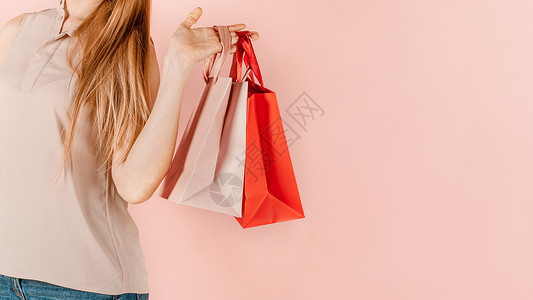 低价购狂欢购物和消费 年轻漂亮的女孩带着纸袋购物 粉红色的背景 节日礼物的选择 为自己购物 小样零售顾客女士销售量中心狂欢微笑购物狂销售购背景