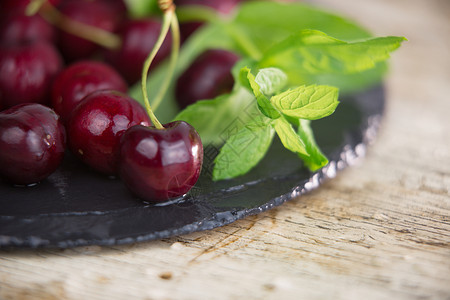 黑色湿岩板黑盘上的新樱桃 在轻木桌上有选择性地聚焦于复制空间的新鲜绿色薄荷收成植物季节桌子食物乡村水果叶子浆果蔬菜背景图片
