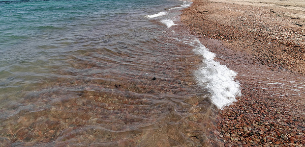 在约旦阿卡巴海滩的小型断裂波 覆盖着粗砂砾石背景图片