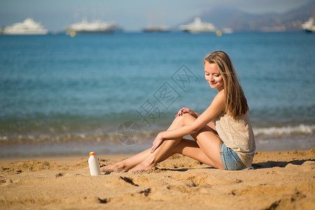 美丽的女人在腿上涂防晒霜海滩护理蓝色天空奶油推杆女士乳液防晒海洋背景图片