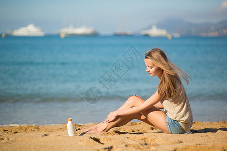 年轻妇女在腿上涂防晒霜女士奶油旅行晴天护理洗剂系数日光浴蓝色身体背景图片