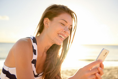 魅族手机带着智能手机的海滩上美丽的年轻女子背景