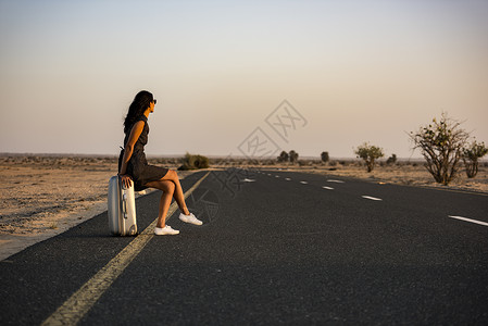 妇女带着行李在沙漠的农村公路上等待着背景