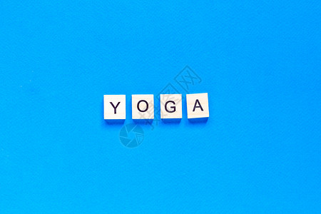 瑜伽班字体YOGA 在蓝色背景 平面布局 顶部视图上以木质纸质格式写成的单词背景