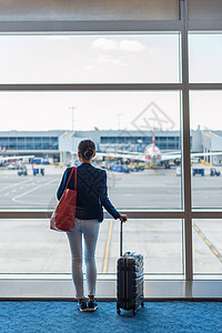 在机场航站楼等待登机的妇女剪影 旅行的女商务人士透过窗户看着停机坪和飞机 商旅理念背景图片
