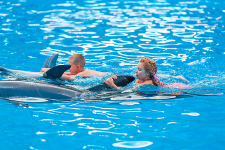 女孩和鲸快乐的小孩和海豚在海豚馆游泳女孩潜水男生野生动物拥抱朋友乐趣疗法假期水池背景