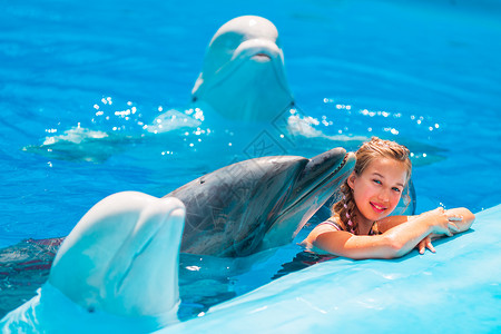 女孩和鲸快乐的小女孩与海豚在海豚馆游泳喜悦荒野童年海洋微笑女孩动物乐趣孩子蓝色背景