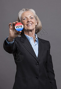 拥有选举竞选活动针头的高级女商务人士的肖像背景图片