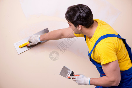 在墙上涂石膏的年轻承包商雇员职业泥水匠涂层工作画家工人装修天花板劳动者男人背景图片