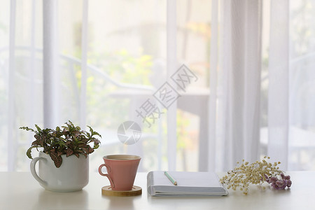 用粉红咖啡杯 白笔记本 蓝铅笔和用窗帘看透的植物来装饰内室内装饰背景图片