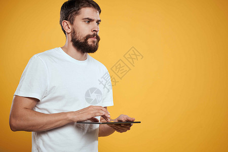 在白色T恤衫上用黄色背景的平板牌男子 商务人士触摸屏幕触摸板的新科技药片展示快乐男人商业成人触摸屏电脑衬衫工作室背景图片