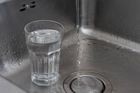 水在金属汇中的饮用玻璃旁边运行 概念高清图片