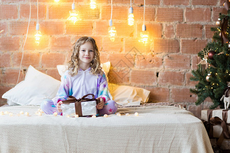 穿着睡衣的可爱女孩坐在床上 打开礼物和新年花冠背景图片